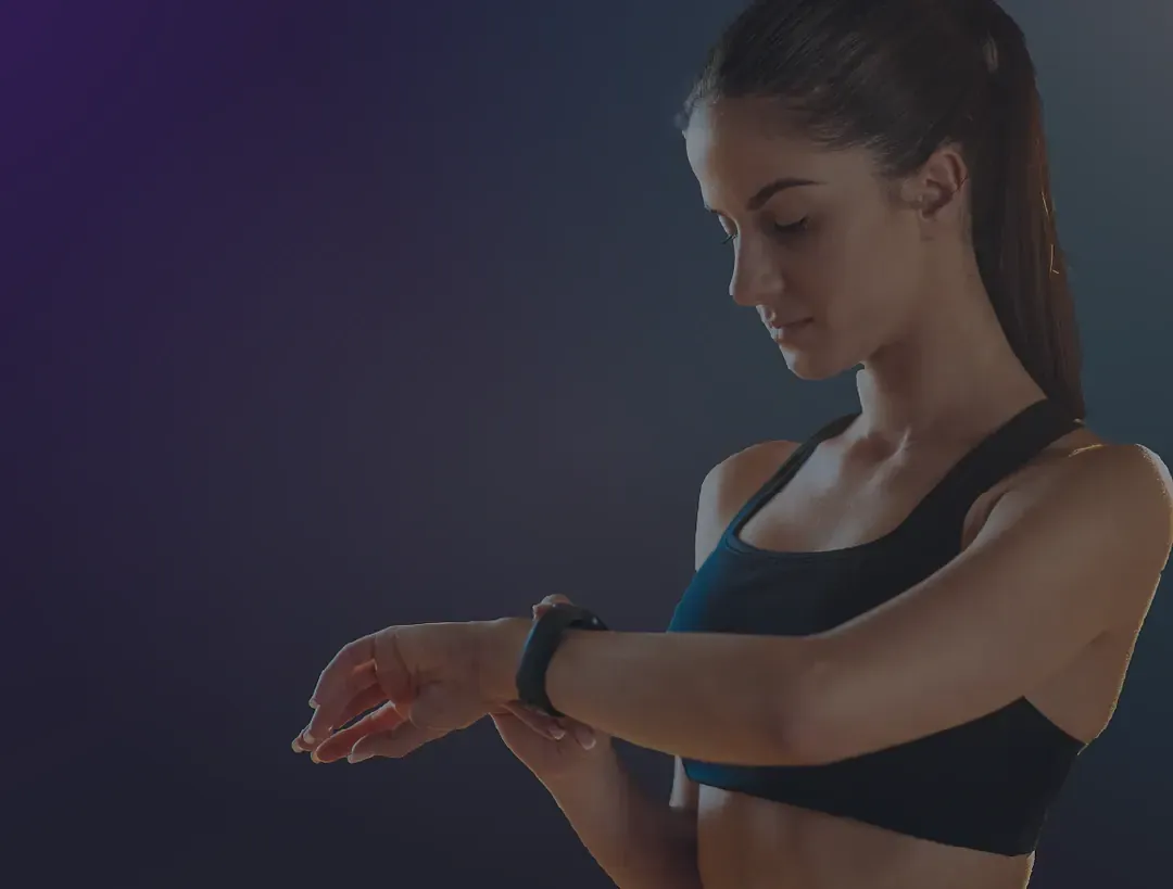 Woman checking the fitness tracker on her wrist against a dark background